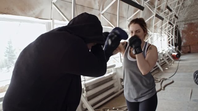 Strong tattooed woman in gloves boxing with male sparring partner while training in gym