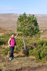 A young woman stands by a small pine tree