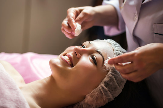 woman getting facial care peeling mask by beautician at spa salon