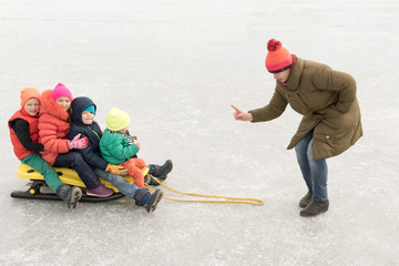 happy children in colorful clothes came with their parents to ride a sled. Emotional children enjoy a sunny afternoon and glide along the frozen lake's ice