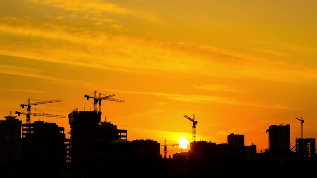 Silhouette of construction site with several cranes working on a building complex with background sunset colors. Construction crews work on high ground heavy industry and safety concept. Zoom in.
