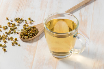 Cup of chamomile tea with dry chamomile flowers  on white wooden background.