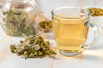 Medicinal tea in glass cup with dried herb.
