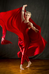 Young woman in red unitard swirling red fabric in studio.