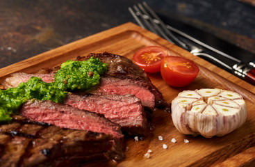 Grilled Black Angus Steak with tomatoes, garlic with chimichurri sauce on meat cutting board.