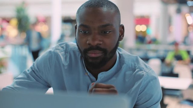 Attractive face african american young man use laptop in cafe concentrated in mall computer web person shopping internet technology black business portrait close up attractive guy sitting slow motion