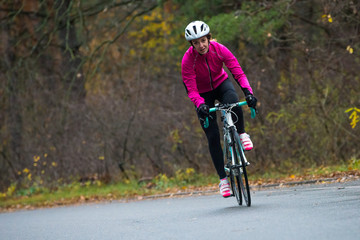 Obraz na płótnie Canvas Young Woman in Pink Jacket Riding Road Bicycle in the Park in the Cold Autumn Day. Healthy Lifestyle.