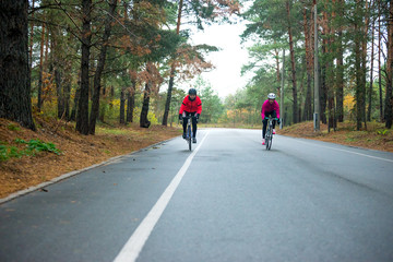 Obraz premium Two Young Female Cyclists Riding Road Bicycles in the Park in the Cold Autumn Morning. Healthy Lifestyle.