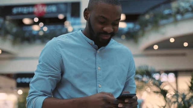 Attractive smiling african american young man using phone standing in shopping center feel happy christmas internet face technology black telephone portrait cute close up mobile holding slow motion