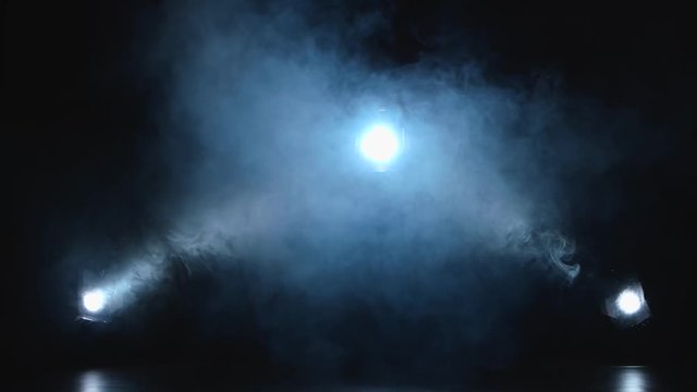 Three white spotlights enveloped in smoke on black background