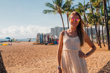 Young girl in a dress walking down the Honolulu Waikiki beach area among palms, surf boards and other people. Honolulu, USA. August 30, 2017