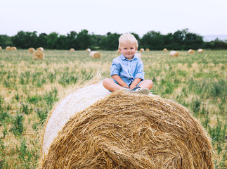 Naklejka na ściany i meble Cute toddler boy sitting on haystacks at wheat field.