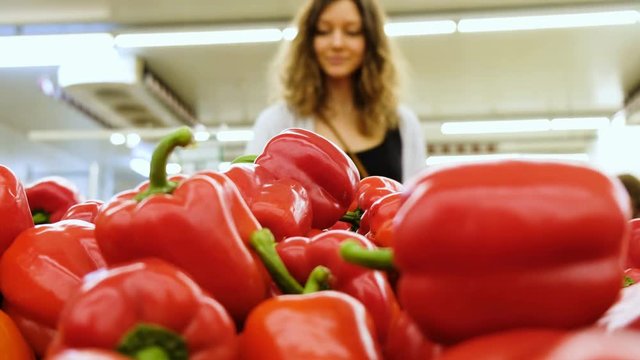 Beautiful girl chooses red pepper in a supermarket, in the blur, 4k.