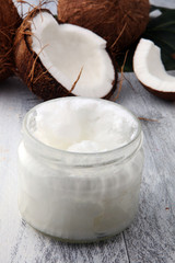 coconut and opened glass jar with fresh coconut oil on wooden background.