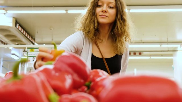 Beautiful caucasian girl chooses a red pepper in a vegetable shop, 4k.