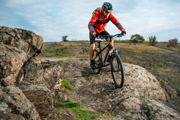 Fototapeta na wymiar Cyclist in Red Riding the Bike on Autumn Rocky Trail. Extreme Sport and Enduro Biking Concept.