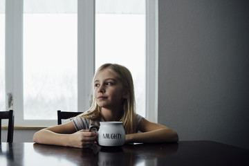 Thoughtful girl holding mug while sitting on chair by table at home