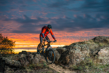 Obraz na płótnie Canvas Cyclist in Red Riding the Bike on Autumn Rocky Trail at Sunset. Extreme Sport and Enduro Biking Concept.