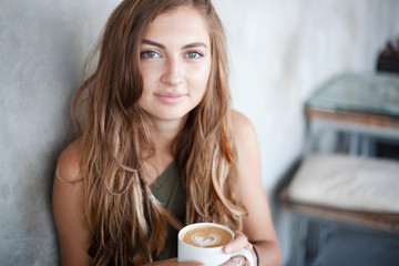 portrait of beautiful girl is sitting in a cafe and holding a mug of coffee