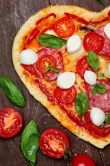Pizza in shape heart with salami, tomatoes, basil and mozzarella against a dark wooden brown background.Copy space.Top View. Creative valentine day background.Love concept.Closeup