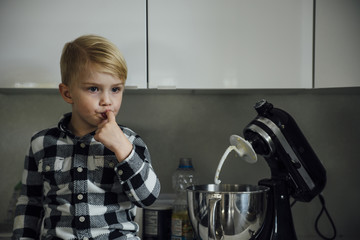 Cute boy tasting food from mixer in kitchen