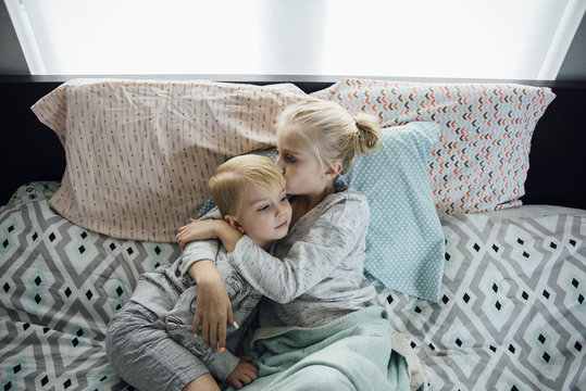 Sister kissing brother while lying on bed at home