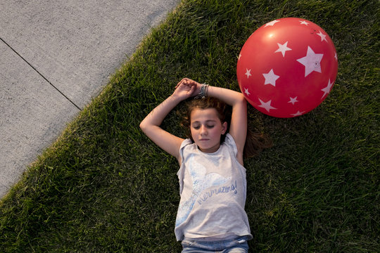 Overhead view of girl lying on grass with balloon at backyard