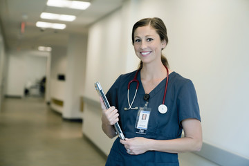 Portrait of cheerful female doctor holding laptop computer while standing in hospital lobby