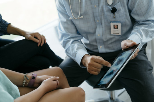 Midsection of pediatrician showing x-ray image on tablet computer to mother and daughter in medical examination room