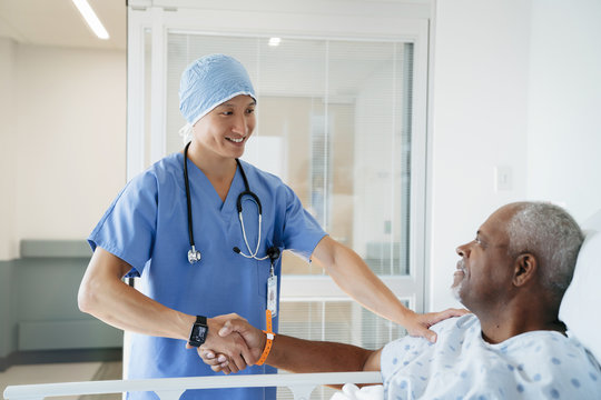 Confident surgeon shaking hands with senior patient in hospital ward