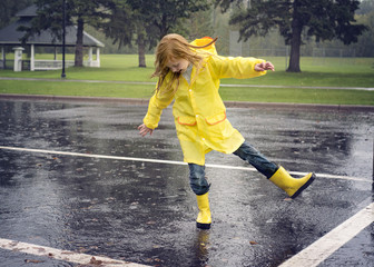 Playful girl wearing raincoat while dancing on road during rainfall