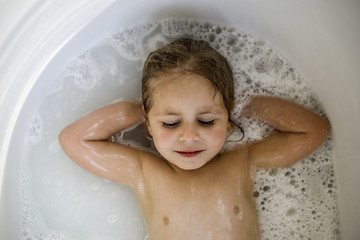 Overhead view of girl with hands behind head lying in bathtub