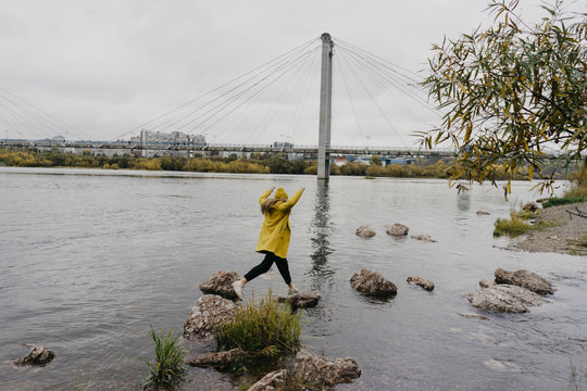 Young Woman Jumping On Rocks In Lake Against Bridge