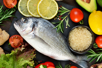 Food background. Fresh, raw Dorado with a swallow, lemon, avocado on a dark concrete background.