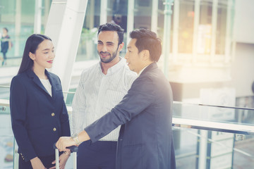 handsome asian young businessman and businesswoman three people in classic suits talking and smile with discussion standing outside the office building, teamwork with business concept.