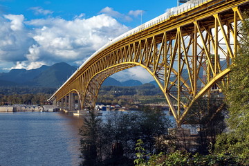 Fototapeta na wymiar The bottleneck of the bay and the yellow metal frame of the transposed bridge Against the backdrop of the mountain ridge and the cloudy sky.