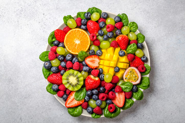 Fruit platter with various fresh strawberry, raspberry, blueberry, tangerine, grape, mango, spinach on a light stone background. Copy space, top view, horizontal