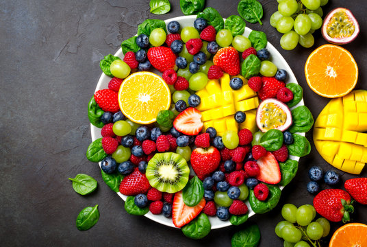 Fruit platter with various fresh strawberry, raspberry, blueberry, tangerine, grape, mango, spinach on a dark black stone background. Copy space, top view, horizontal image