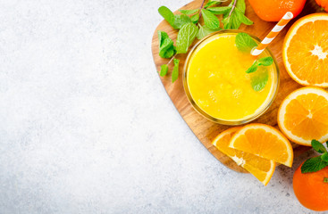 Un verre de jus d& 39 orange fraîchement pressé avec une paille et des feuilles de menthe sur une planche en bois et un fond en pierre clair. Vue de dessus, image horizontale, espace de copie