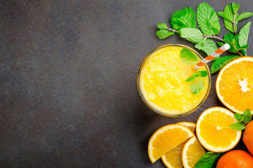 One glass of freshly pressed orange juice with a straw and mint leaves on a dark black stone background. Top view, horizontal image