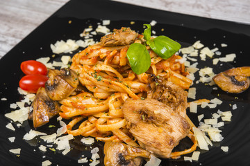 Pasta in a black plate on light wood. Tagliatelle with .mushrooms
