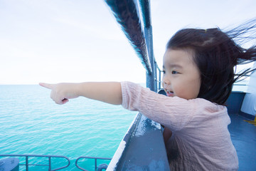 Happy asian baby girl hanging on metal fence and pointing finger in ferry ship to samui island...