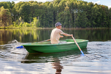 A fisherman with fishing rods is fishing in a wooden boat against the backdrop of beautiful nature and lake or river. Camping tourism relax trip lifestyle concept