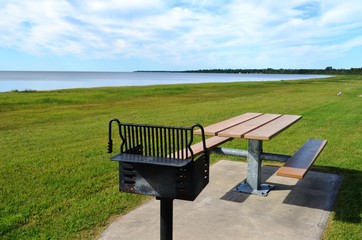 BBQ grill and picnic table at a grassy  waterfront park on a sunny summer day