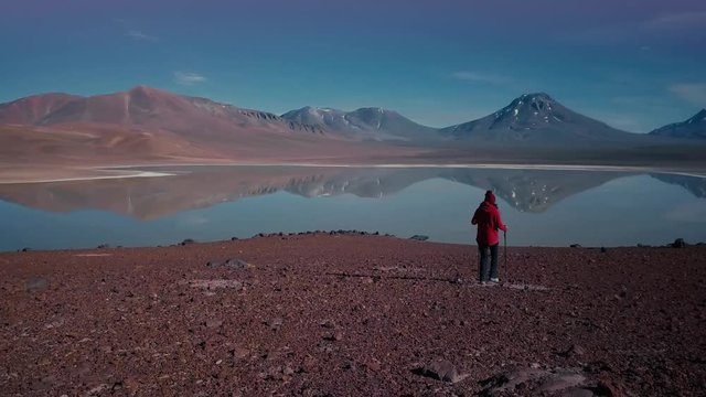 Hiker woman wearing a red hood walking down the hill. Aerial view of mountain lake panorama in the Atacama desert. 