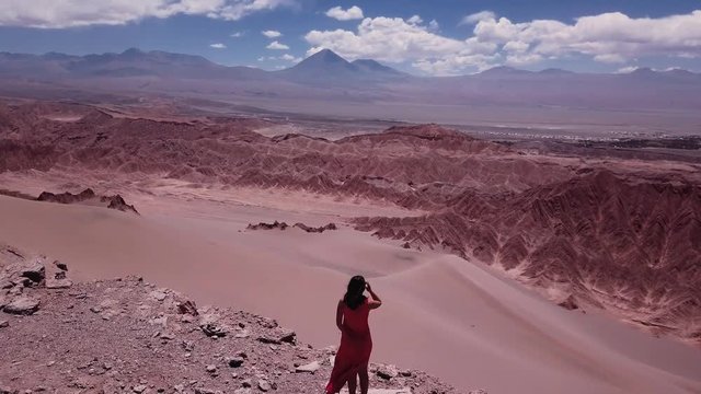 Aerial view of woman wearing a red dress standing over the edge of a sand desert, Dead Valley, Chile. 4k