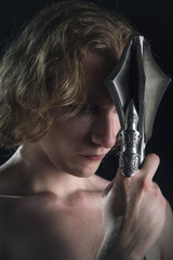 Young valiant knight looking man with rich blond curls holding a steel mace, black background