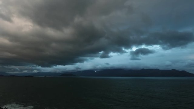 Ocean waves lapping across the south china sea with mountains and cloudy dramatic skies high definition time lapse movie footage.