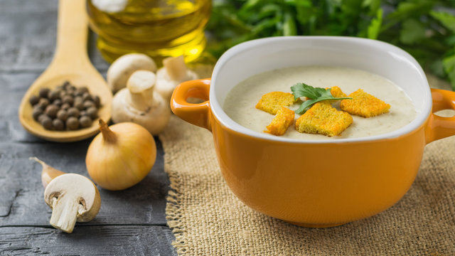 Freshly prepared cream soup of mushrooms with croutons and herbs on a wooden table.