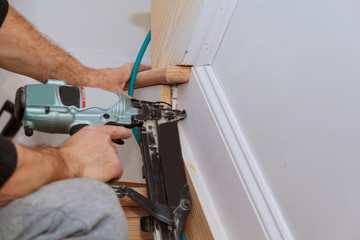 Carpenter brad using nail gun to Moulding trim, with the warning label that all power tools